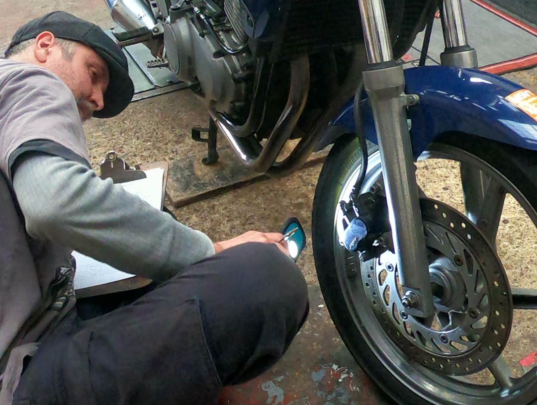 MoT Tester checking brake pads on a motorcycle