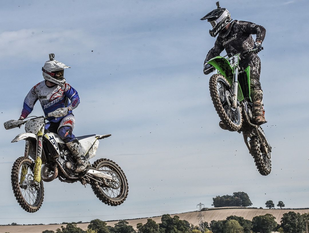 Two motocross riders side by side in mid air looking at each other