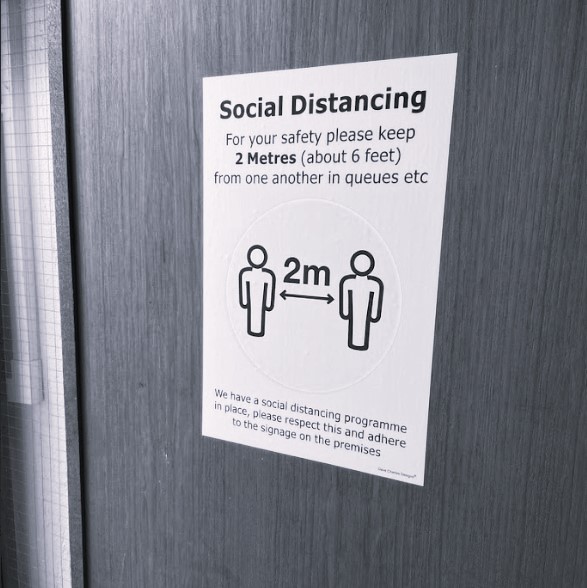 About BeMoto – Social Distancing A black and white photo of a social distancing sign fixed to an office door. The sign explains the importance of keeping a suitable distance apart to limit the chance of spreading Coronavirus.