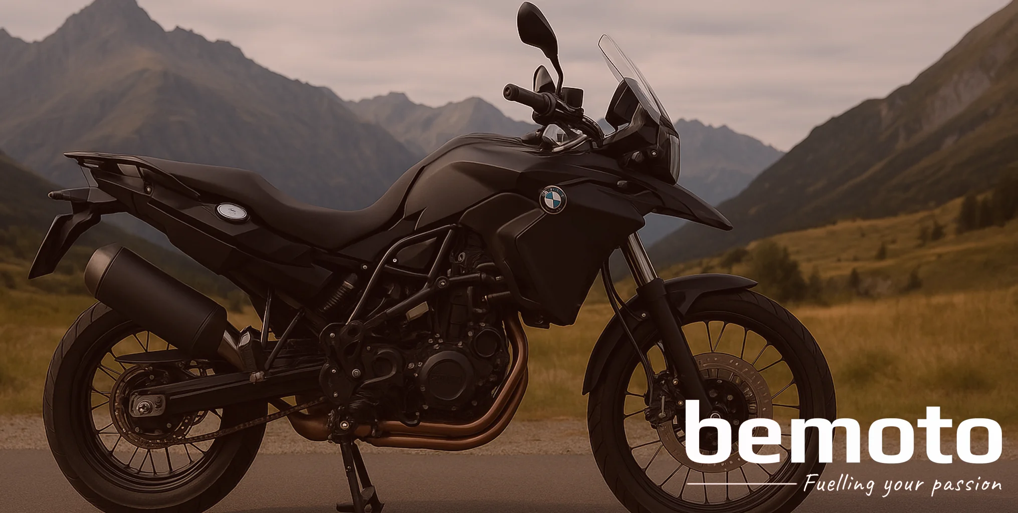 A matte black BMW F 450 adventure bike is parked on a mountain road, resting on its sidestand. Jagged peaks and rolling green valleys sit in the background under an overcast sky, giving the scene a rugged touring atmosphere.
