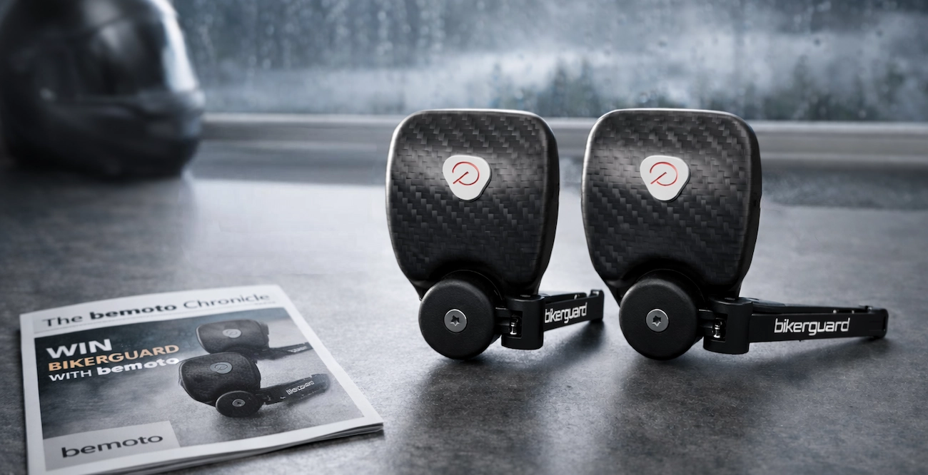 Two BikerGuard wiper units displayed on a kitchen worktop with a rainy window and motorcycle helmet in the background, alongside a BeMoto magazine titled “Win BikerGuard with BeMoto”.