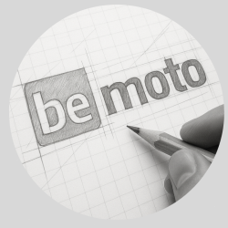 About BeMoto – Logo Creation Hand-drawn sketch of the BeMoto logo in development, featuring the word "be" inside a shaded square and "moto" in lowercase beside it, all on graph paper with construction lines and a pencil in hand—illustrating the creative process behind the logo's clean, modern, and balanced design.